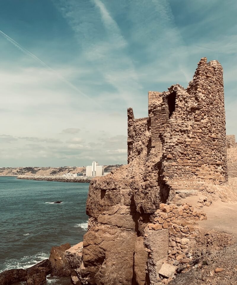 Photo by Imad El ouazzani an old stone building sitting on top of a cliff next to the ocean